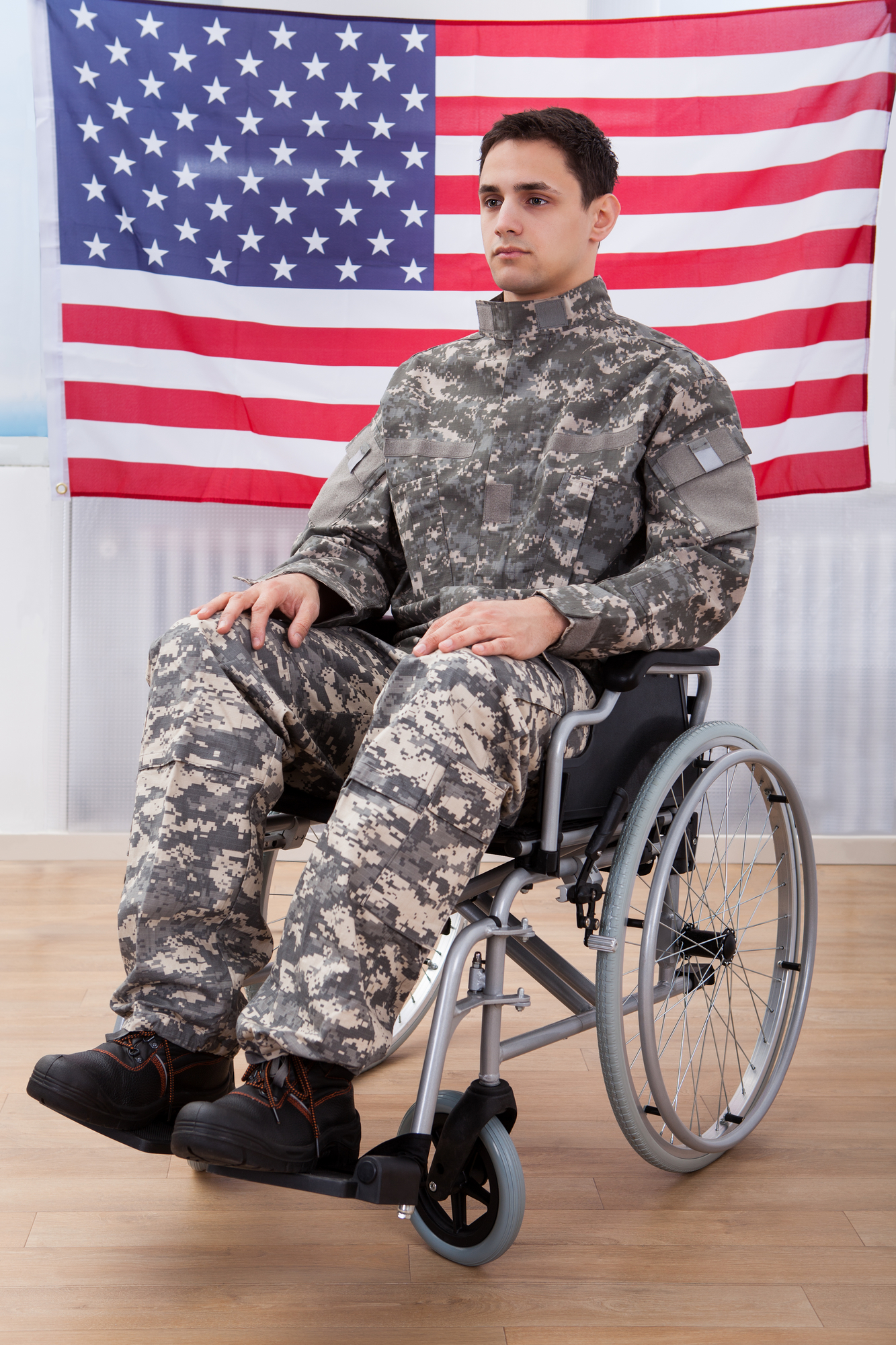 Patriotic Soldier Sitting On Wheel Chair Against American Flag