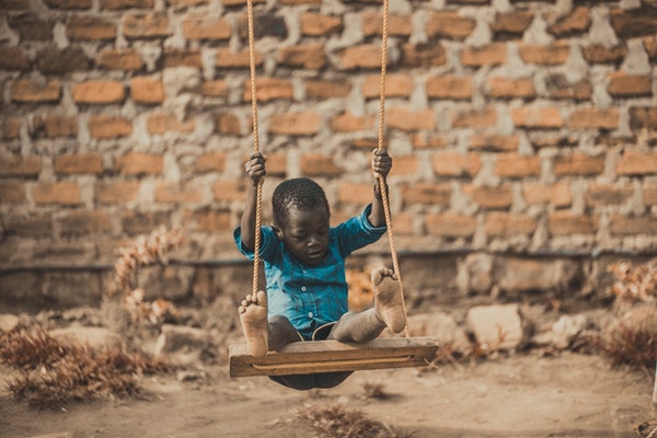 African boy wearing blue shirt sitting on swing