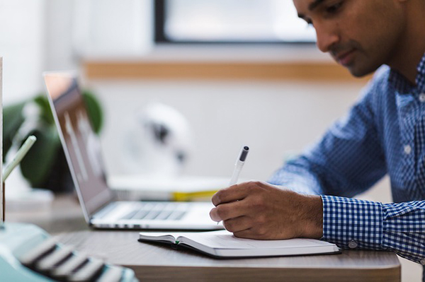 Man writing near a laptop