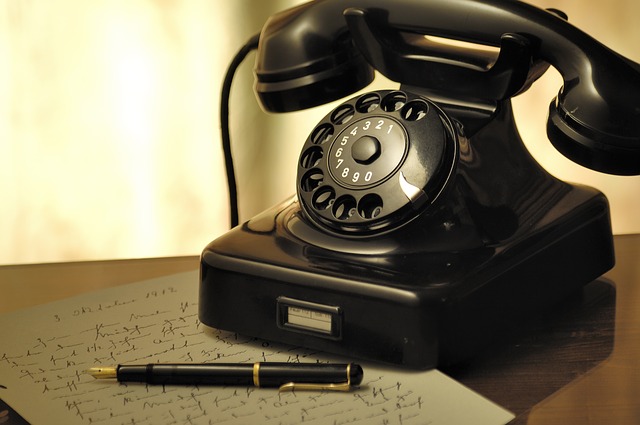 a vintage telephone with rotary beside a letter and a pen