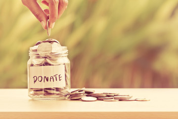 Hand putting Coins in glass jar for giving and donation concept - feed my starving children